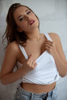Young sexy brunette wearing white top and jeans giving a seductive look shot against brick wall