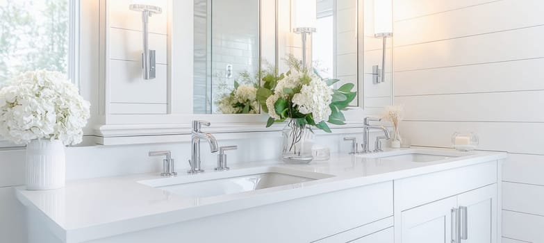 Luxurious white bathroom vanity is illuminated by modern chrome fixtures and decorated with fresh white hydrangeas