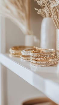 Elegant golden bracelets arranged on a white shelf, adding a touch of glamour to a room decorated with dried flowers