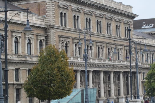 An impressive building with intricate stonework and large windows stands prominently in a city, showcasing its grandeur despite the cloudy sky.