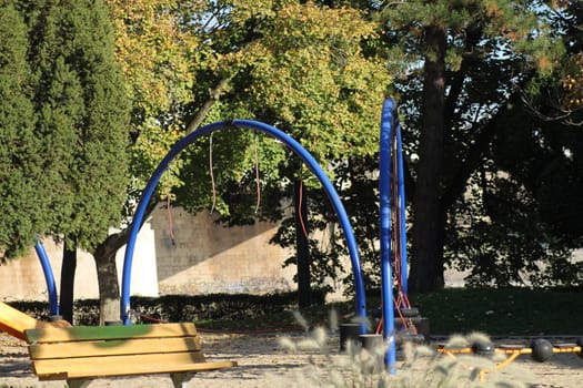 A vibrant playground features colorful swings and a slide nestled among lush trees, inviting children to play in the warm sunlight of a clear day.