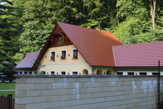 A picturesque house featuring a vibrant red-tiled roof is nestled among dense greenery. The setting offers a peaceful retreat from urban life, showcasing nature's beauty.