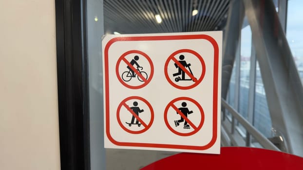 Sign on glass with 4 symbols prohibiting use of personal transport when entering public place, ban on use of bicycle, scooter, skateboard and roller skates with special sign for safety reason
