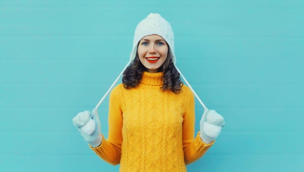Winter christmas portrait of happy young woman smiling in yellow sweater, white hat standing on blue background