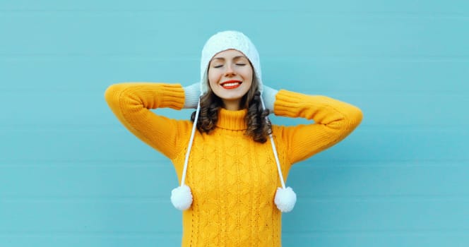 Winter christmas portrait of happy young woman smiling dreams in yellow sweater, white hat on blue background