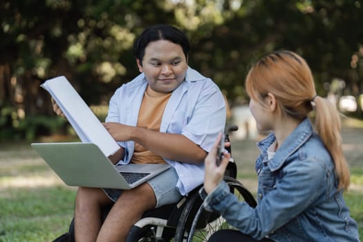 A young man in a wheelchair works on paperwork with a friend in a park, showcasing teamwork and accessibility.