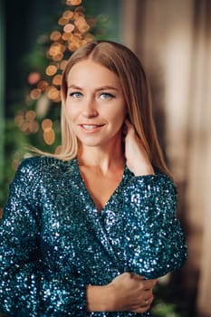 woman in a green sequined dress holding a present box near a Christmas tree smiling,