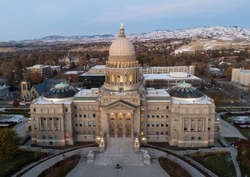 The Capitol building is a large, ornate structure with a dome on top. The surrounding area is mostly empty, with only a few cars and a few people visible. The sky is a mix of blue and orange