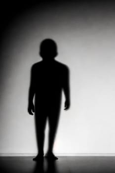 A silhouette or shadow of a man standing in front of a wall. The image has a moody and mysterious feel to it