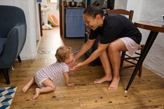 A loving mother interacts with her crawling baby on a wooden floor in a warm, homey atmosphere, showcasing family care.