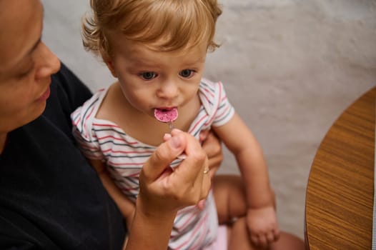 A mother lovingly feeds her baby a healthy snack at home. The baby looks curious and engaged, highlighting the nurturing bond and care between them in a warm, family environment.