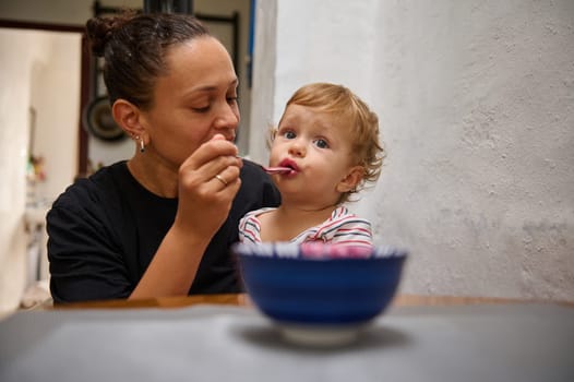 A caring mother gently feeds her toddler in a warm, intimate home environment. The child appears curious and content, fostering a tender family bond and nurturing moment.