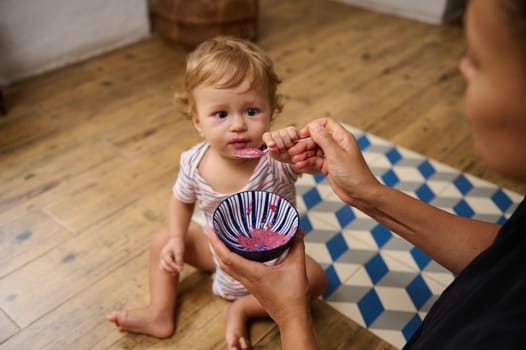 A mother gently feeds her baby using a spoon, creating a nurturing moment in a cozy kitchen setting. The baby looks curious and engaged, enjoying the mealtime experience.