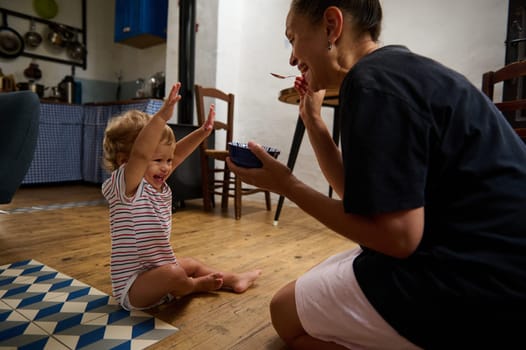 A happy toddler gleefully playing on a kitchen floor, with an adult sharing laughter and a snack. Their joyful interaction captures the warmth and love of family bonding moments.