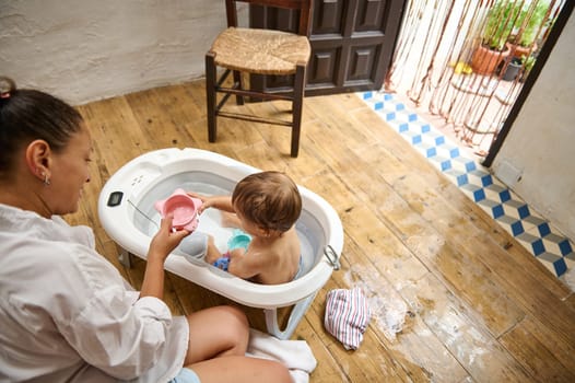 A joyful mother helps her baby during bath time at home, creating a warm and nurturing environment. The scene depicts a relaxed, everyday moment filled with care and love.