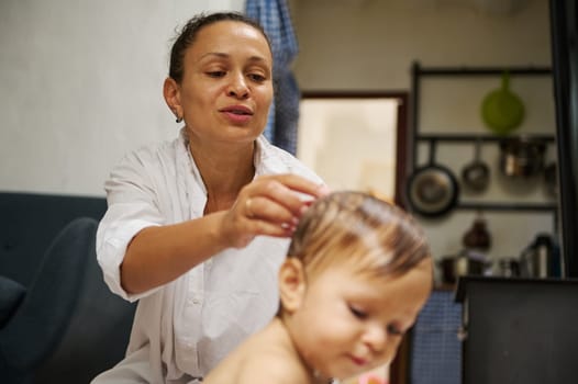 A mother gently dries her toddler's hair in a warm kitchen setting, showcasing maternal care and bonding. The scene conveys love, family, and home life.