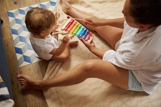 A mother and her young child share a joyful moment playing the xylophone together, creating a warm and nurturing atmosphere in a cozy home setting.