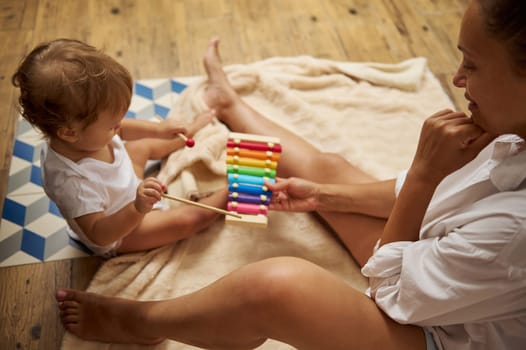 A mother and her child enjoy quality time together, playing with a bright xylophone. The child learns through play, exploring sounds and colors in a homey setting. Warm, nurturing atmosphere.