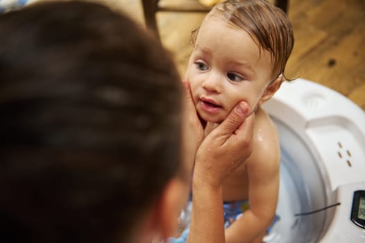 A tender moment of a mother bathing her baby in a tub, wrapped in love and care. The warm home environment and gentle touch evoke feelings of comfort, safety, and affection.