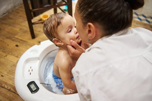 A mother lovingly bathes her baby in a white tub, showcasing tender care and family bonding in a cozy home setting.