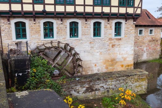 a charming historic watermill adjacent to a stone building, surrounded by lush greenery and vibrant flowers, reflecting a serene and rustic atmosphere in steinfurt germany