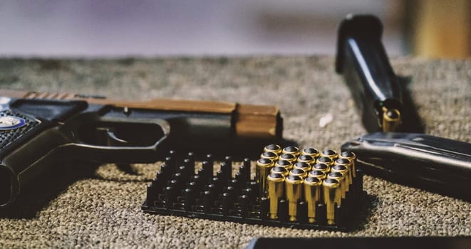The image shows a handgun, ammunition, and a magazine. The ammunition is arranged neatly in a tray holder. The handgun and the magazine appear to be placed on a surface, possibly a table or countertop.