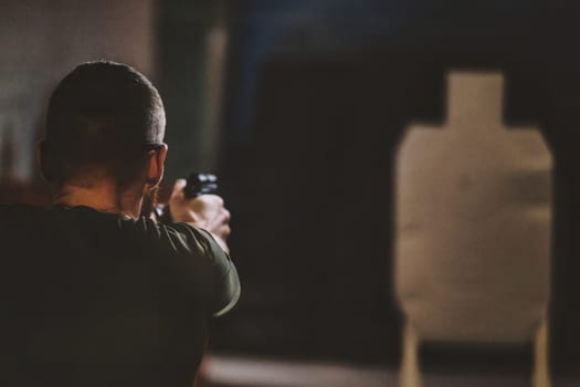 The image shows a person aiming a firearm toward a target at what appears to be an indoor shooting range. The person is seen from behind, focusing on the target in front of them. The target is shaped like a human silhouette and is positioned at some distance from the shooter. The scene is likely set in a controlled environment intended for shooting practice.