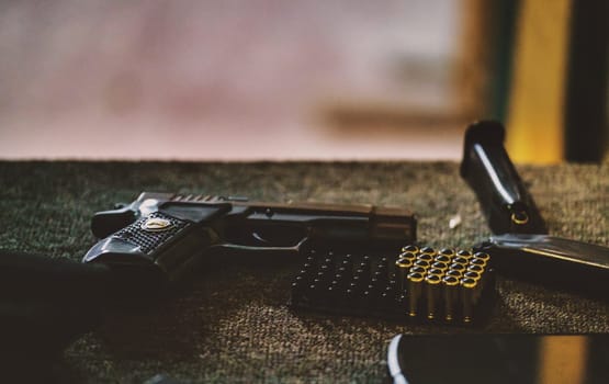 The image features a handgun along with a few rounds of ammunition and a magazine. The setting appears to be an indoor environment, possibly a shooting range or an area where firearms are handled and maintained.