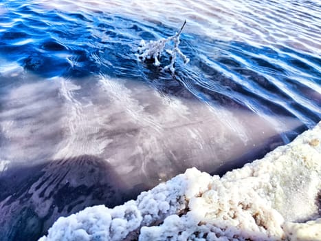Salt accumulates along the shoreline of a calm salt lake, reflecting clear blue skies and creating picturesque natural beauty.