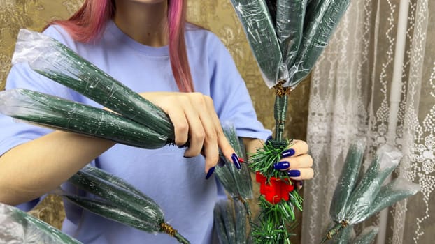 Girl hands installs branches of artificial Christmas tree on wire into the trunk to decorate her home for the New Year. Decorating for Christmas with folding artificial New Year tree