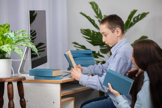 A young boy and a girl focus incredibly intently on their study materials laid out at a desk with a computer setup