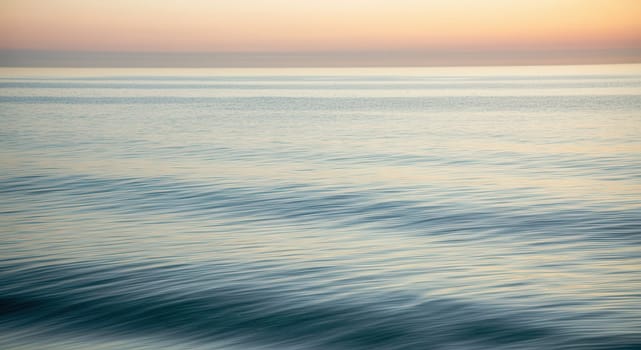 Serene ocean waves ripple under a tranquil sunset, showcasing soft pastel hues of the sky meeting the reflective sea. ideal as a calming background for design projects or prints, emphasizing peace and natural beauty.