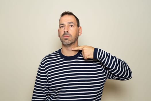 A bearded Hispanic man threatens to cut his throat. The man has a violent look and makes threatening gestures. The man threatens and looks for a fight