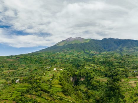 Aerial view of farmland with plantings against a background of mountains and blue sky. Kanlaon volcano. Negros, Philippines