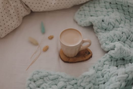 Cup of coffee with milk on the bed with white linens and blanket. Morning coffee in bed concept