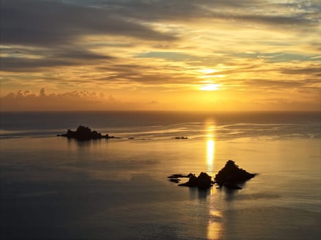 Bright orange sun rising over the beach town of Oakura, New Zealand. Silhouetted rocky islands and outlets frame the serene and tranquil scene