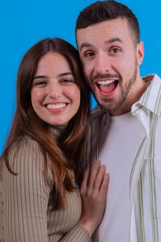 A joyful young couple embracing and smiling warmly at the camera against a vibrant blue background. Ideal image for love, relationships, happiness, or positive lifestyle concepts.
