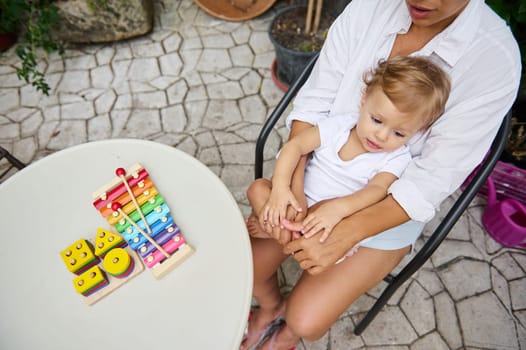 A mother and her young child enjoy playtime outdoors with vibrant toys on a table. The scene exudes warmth and nurturing, capturing a moment of family bonding and development.