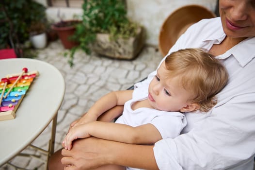 A tender moment between a mother and her child sitting outside on a patio. The child looks content in the mother's arms, while a colorful xylophone sits nearby, enhancing the cheerful atmosphere.