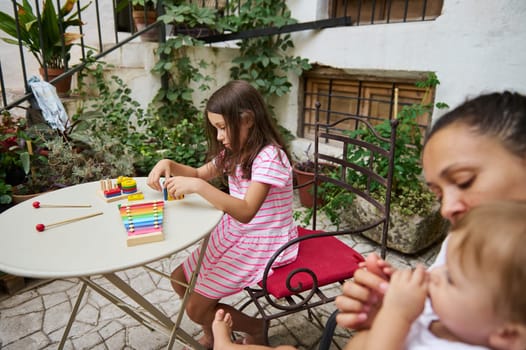 Young girl enjoys playing a colorful xylophone in a cozy garden patio setting with her family nearby.