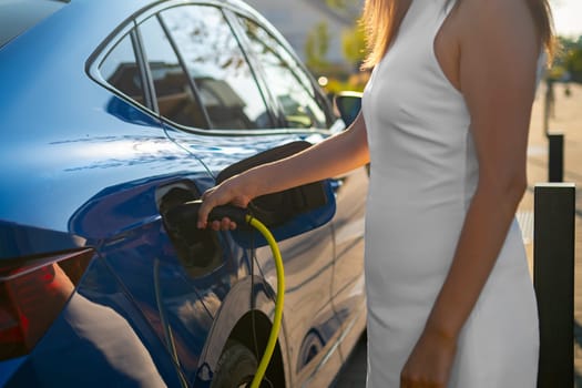Close up woman in a white dress connecting an electric car to a charging station on a city street