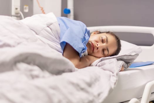 Young woman in blue robe lying comfortably and getting ready for bed on hospital bed in calm environment of clinic in private room, soft lighting, concept of recovery and care,