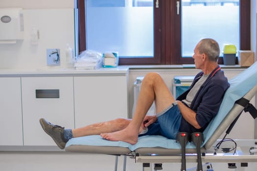 middle aged man sits deep in thought on a medical couch in a clinic office, waiting for the doctor to examine him and put a cast on his broken leg, professional first aid concept,