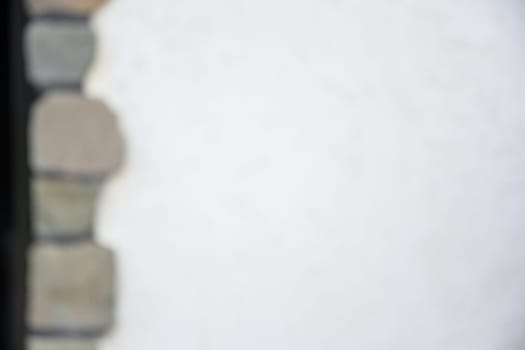defocused image, The wall of the house is covered with white relief plaster and decorated along the edge with masonry made of natural gray stone, abstract textured background, surface in blur,