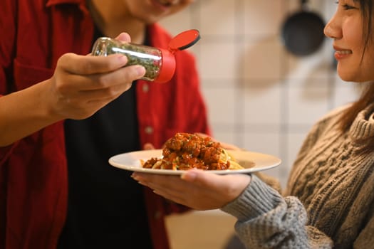 Close up of man garnishing a plate of freshly prepared pasta with dried herbs.