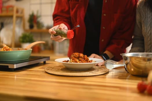 Close up of man garnishing a plate of freshly prepared pasta with dried herbs.