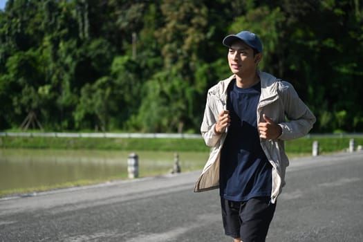 Active young asian man jogging by a riverside path on sunny day.