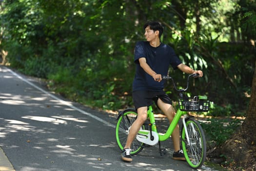 Young man riding a bicycle along narrow dirt path in a green park on sunny day. Outdoor activities concept.