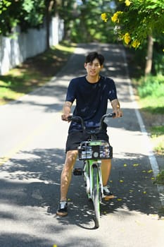Active man riding a green bicycle on tree lined road on a sunny day. Outdoor activities concept.