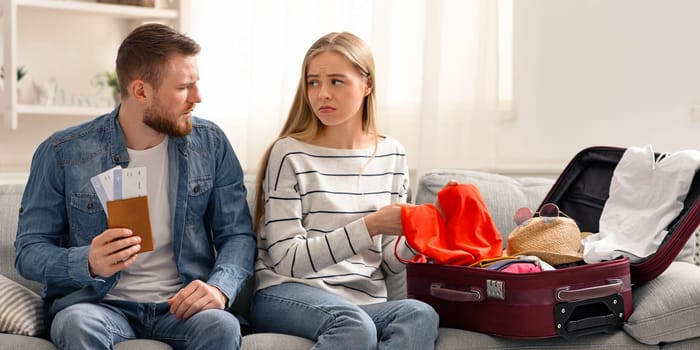 Vacation disaster. Sad couple suffering unpacking suitcase for trip at home, empty space